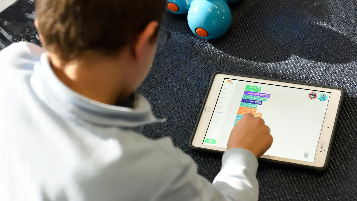 A child using a learning app on a tablet, with a coding robot beside them.