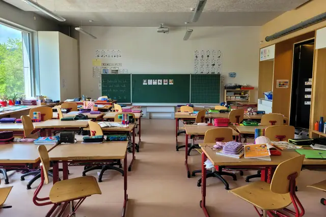 An empty primary school classroom with small chairs stacked beside low desks.