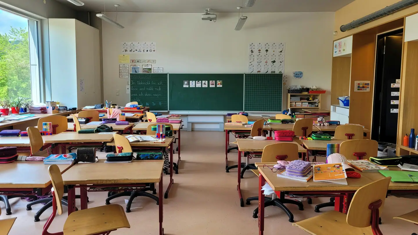 An empty primary school classroom with small chairs stacked beside low desks.