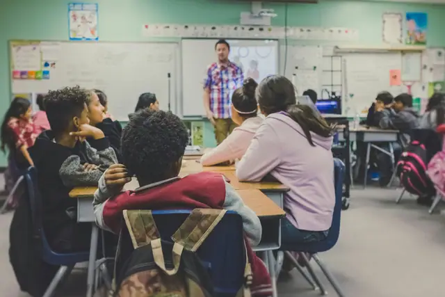 Teenage students seated at tables in a bright high school classroom during a lesson.