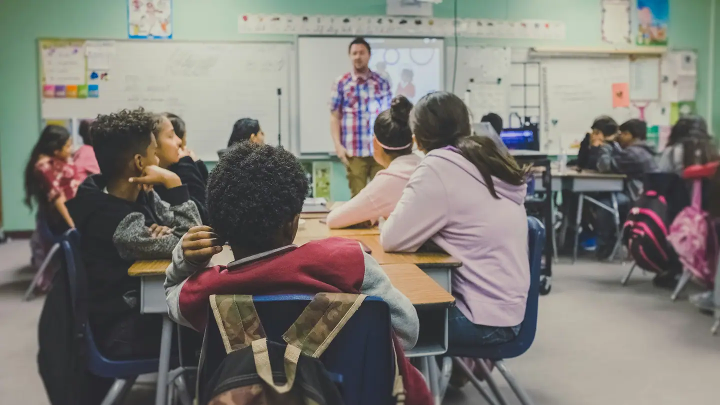 Teenage students seated at tables in a bright high school classroom during a lesson.
