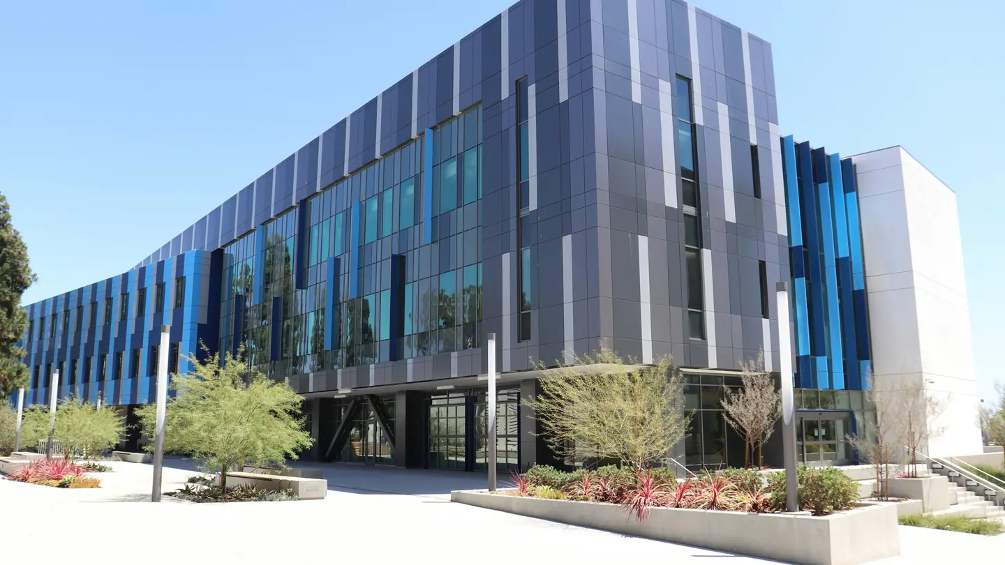 A modern research building clad in glass and dark metal panels seen from the street.