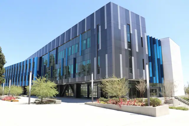 A modern research building clad in glass and dark metal panels seen from the street.