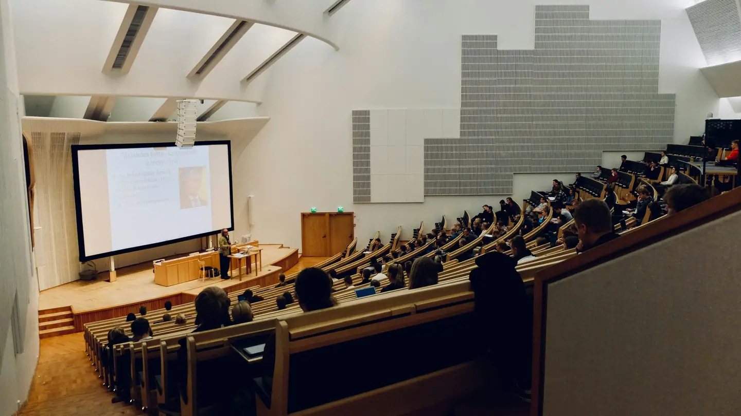 A raked university lecture theatre with rows of desks facing a projection screen.