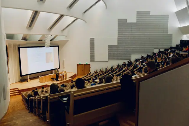 A raked university lecture theatre with rows of desks facing a projection screen.